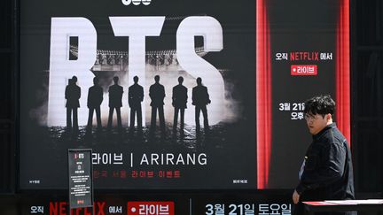 A man walks past a truck promoting the comeback concert of K-pop boy group BTS in Seoul on March 19, 2026. BTS, the world's biggest boy band, reunites on stage on March 21, in a K-pop extravaganza watched by hundreds of thousands of fans in downtown Seoul and by millions around the planet online. (Photo by Jung Yeon-je / AFP) (JUNG YEON-JE / AFP)